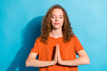 Portrait photo of youngster cheerful girl with beautiful curly red hair wearing orange t shirt praying calm isolated on blue color background