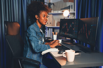 Young African American businesswoman concentrating on dynamic stock exchange market graph monitoring screen laptop, wearing jeans shirt. Concept of investment currency or asset blogger. Tastemaker.