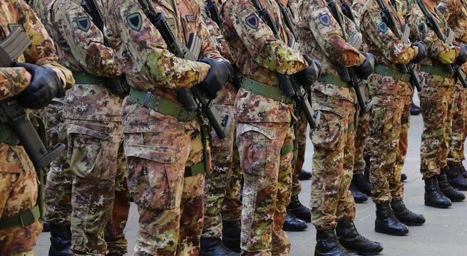 many soldiers in camouflage uniforms standing at attention with assault rifles