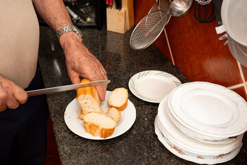 A man is cutting bread on a plate. The plate is on a counter next to a pile of plates