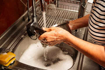A woman washes a dirty dish in a sink. The sink is full of soapy water and the woman is using her...