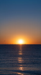 Idyllic sunrise with the bright sun emerging on the sea horizon beautifully illuminating the calm blue waters of the Mediterranean Sea with silhouettes of fishing boats and seagulls on the horizon.