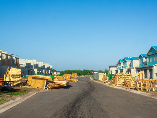 Perspective of a new asphalt street lined with townhouses under construction, with stacks of wooden trusses for building roofs, in a suburban residential development in southwest Florida