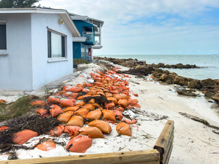 Sandbags laid along a narrow sand beach between row of boulders and small beach houses on a barrier...