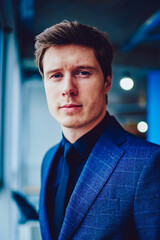 Half length portrait of concentrated male manager in formal apparel looking at camera and waiting meeting with colleague in office,caucasian confident businessman in elegant suit standing in workspace