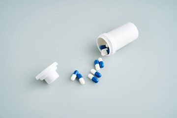 Blue and white capsules spilled out of a medicine jar on a blue background.