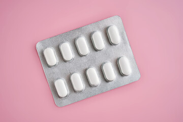 Open pack of pills on a pink background.