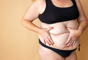 Overweight woman with fat body in underwear posing on beige studio background. Concept of body...