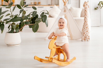 smiling baby girl sitting on a wooden rocking horse in white clo