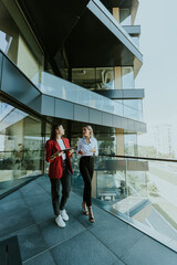 Two businesswomen discuss strategy outside modern office building in daylight