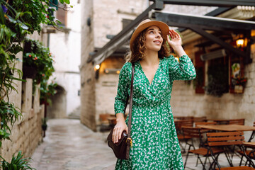 Happy curly woman wearing trendy summer outfit walking in street of European city. Fashion, lifestyle concept. Travel, tourism.