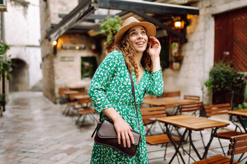 Happy curly woman wearing trendy summer outfit walking in street of European city. Fashion,...
