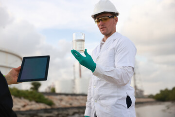 Ecologists in protective suits working near the oil refinery  and taking samples of water for...