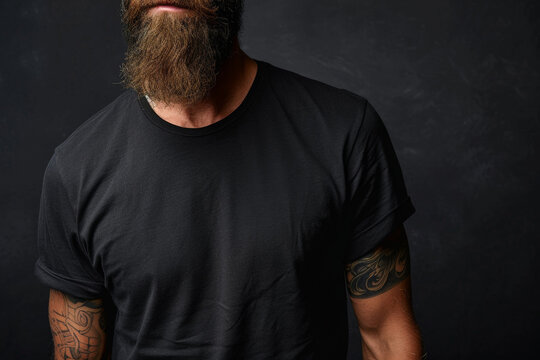 A man in black t-shirt with a beard and tattoos strikes a pose for a portrait, mock up