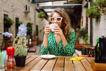 Young woman tourist drinks coffee in the old town in summer trip. People, fashion, lifestyle, travel and vacations