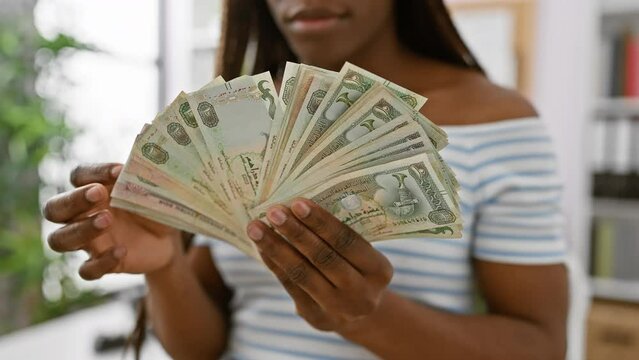 African woman in striped top displaying uae dirhams indoors, symbolizing economy and finance.
