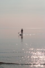 A lone paddleboarder, silhouetted against the serene sunset waters, embodies peaceful solitude in...