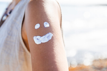 A woman has a smiley face drawn on her arm with white cream, summertime mood