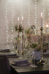 Glasses, plates and candles are on the table. Lots of lights in the background.
