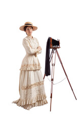 Young woman in Victorian dress with a straw hat standing by a camera on a tripod