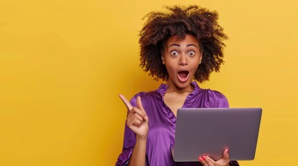 Young woman holding a laptop and pointing her finger to the side, against a yellow background, wearing a purple blouse, with curly hair, a surprised expression, open mouth, looking at the camera