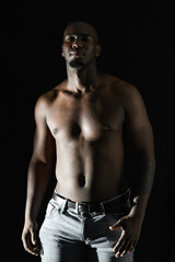black african american man posing shirtless on a black background, looking straight ahead. 90...