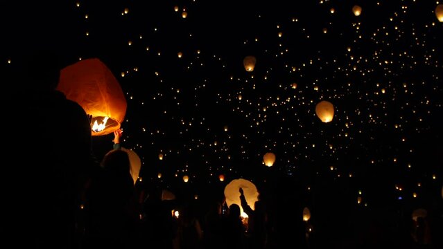 Silhouette of crowd releasing Chinese lanterns into night sky
