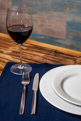 Fork and knife beside a plate on a blue cloth, with a glass of red wine, on a restaurant table.