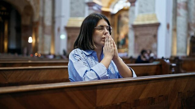 Young beautiful hispanic woman praying on a church bench at St. Karl Borrom&auml;us church