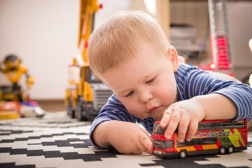 Cute little baby boy playing with toy bus in his room. Indoors activities with children. Child playing in kid's room.