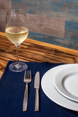 Fork and knife beside a plate on blue cloth, with a glass of white wine, creating an elegant...