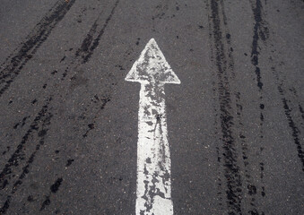 white painted pointing arrow on asphalt road with wet tyres tracks.