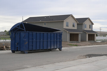 Large blue construction dumpster in front of new duplex homes under construction.