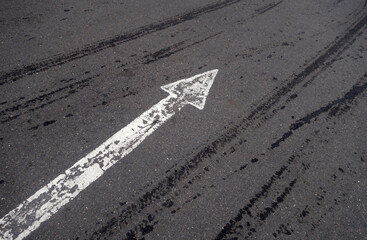 white painted pointing arrow on asphalt road with wet tyres tracks.