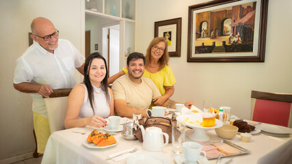 família em casa sentada a mesa pra tomar café da manhã, reunião de família, família feliz comendo. mesa de café da manha com frutas e pão.