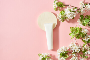 Mockup white cream tube and spring flowers on a pink background