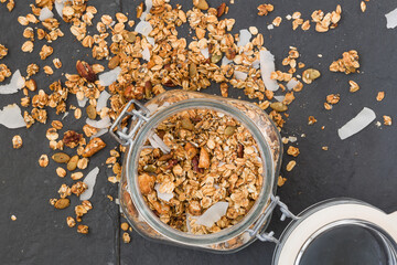 Glass jar of homemade organic granola with coconut and pecans on black background. Delicious breakfast cereal. Healthy muesli.