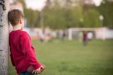 Fototapeta premium Little soccer player standing in the goalposts defending the the line and ready to throw a football. Cute kid boy standing as goalkeeper on a sportsfield on a sunny day. Sport activities for children