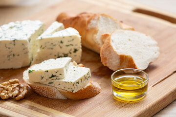 Variety of home made cheese and herbs, olive oil, and bread on a wooden board. Brined curd white cheese with vegetables on the table