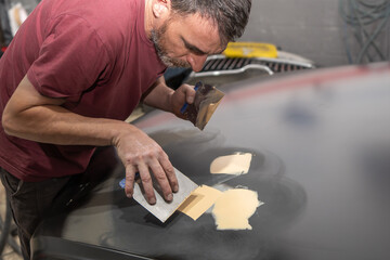 Auto Mechanic Smoothing Body Filler on Car Surface