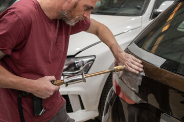 Mechanic Repairing Dent on Rear Car Door with Electric Dent Puller