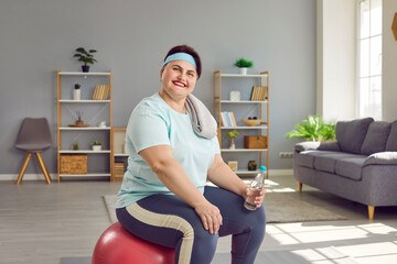 Funny happy young smiling fat woman wearing sportswear sitting on a fit ball with a bottle of water...