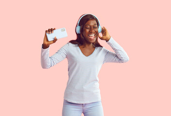 Happy cheerful joyful African woman in noise cancellation headphones head set on pastel studio...