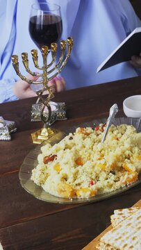 A Jewish woman in blue at the Pesach Seder table reads kiddush with a glass of wine. Vertical video