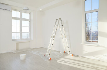 Step ladder, paint bucket and piece of floor protective film in corner of modern living room with...