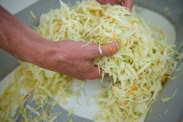Close-up view from above of hands of a chef man mixing raw fresh chopped cabbage, seasoning and...