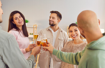 Group of young friends toasting wine glasses and talking standing in a circle together at home. People cheering with glass of champagne celebrating birthday at home party. Celebration concept.