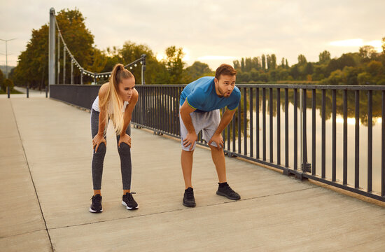 Portrait of a young tired couple man and woman wearing sportswear having a rest after fit sport exercises or jogging in the park outdoors. Workout in nature, fitness training concept.