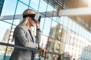 Young businesswoman wearing virtual reality headset simulator outside modern office building. Young...