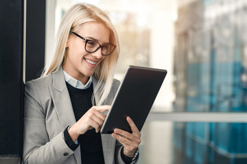 CEO female white collar worker with glasses using digital tablet while standing outside the office.